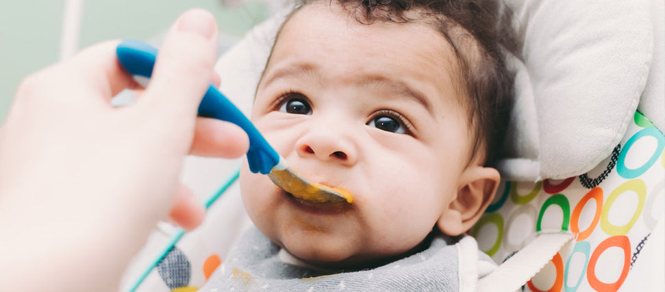 baby being spoon fed by mother's hand