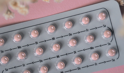 birth control pills on pink background with flower petals