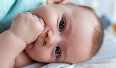 baby with hand on mouth lying in crib 