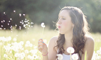 woman blowing dandelions in field