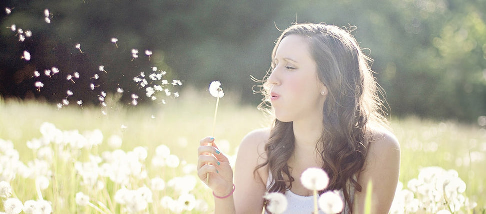 woman blowing dandelions in field